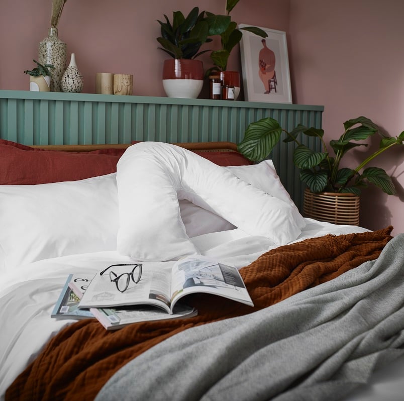 The Arinta Organic Cotton V-Shaped Pillowcase in white on a V-pillow that is in the center of a dressed bed.