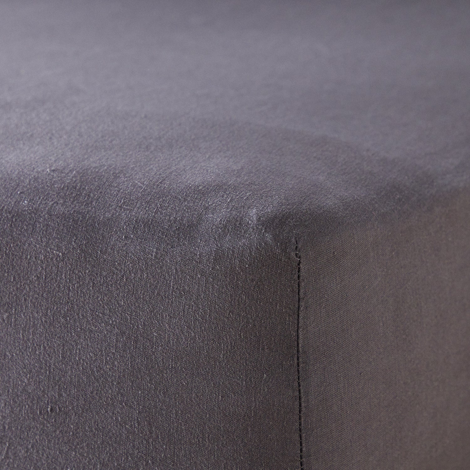 A close up of the corner of a mattress with Woolroom's Mariana Linen Blend Fitted Sheet in Charcoal.