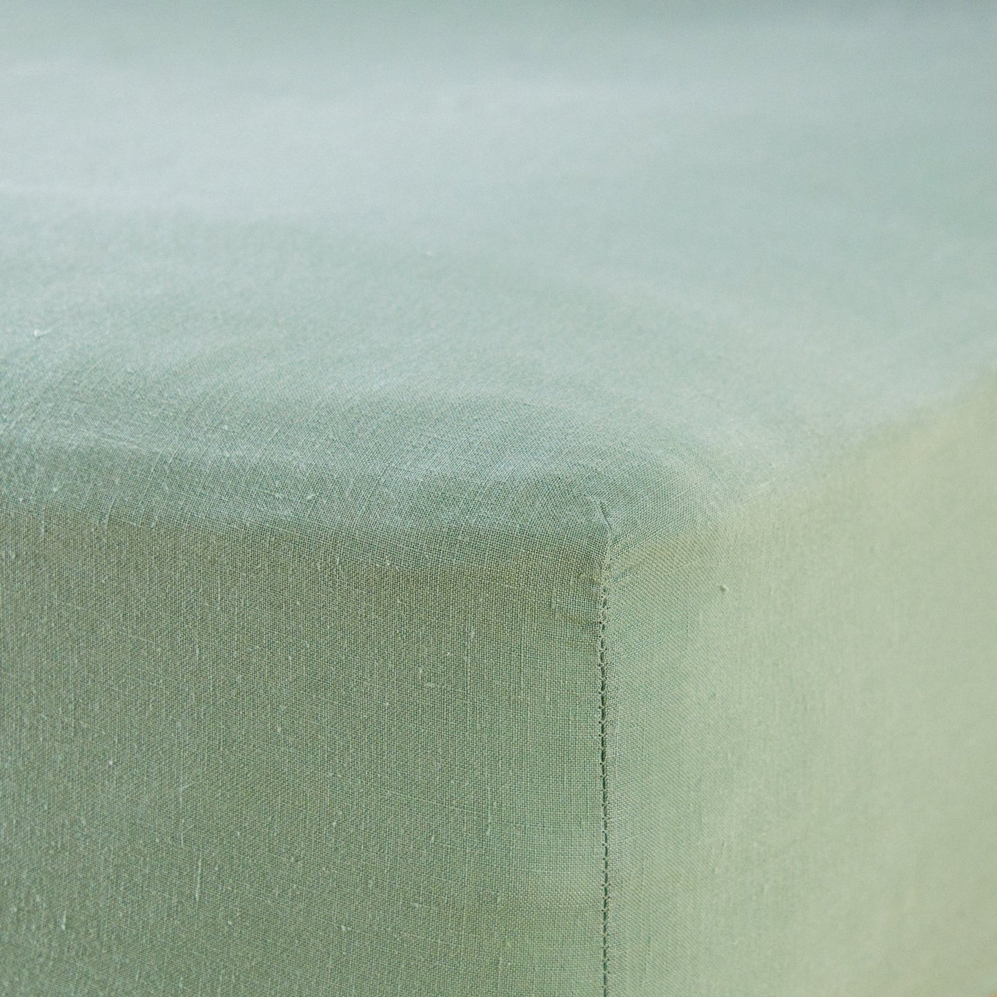 A close up of the corner of a mattress with Woolroom's Mariana Linen Blend Fitted Sheet in Sage.