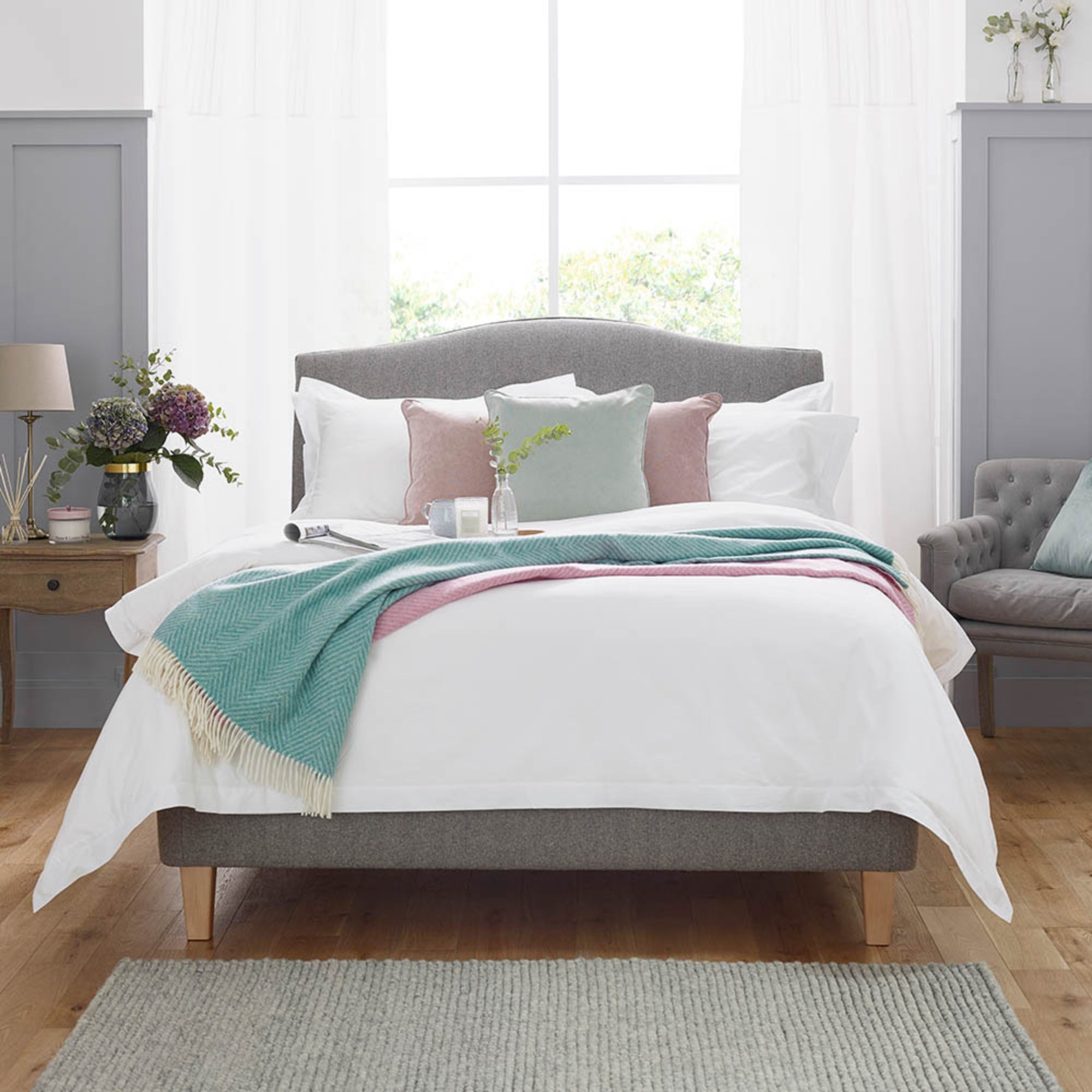 The Isabella Upholstered Bedstead in a fully custom fabric combination, fully dressed with throws blankets and pillows.