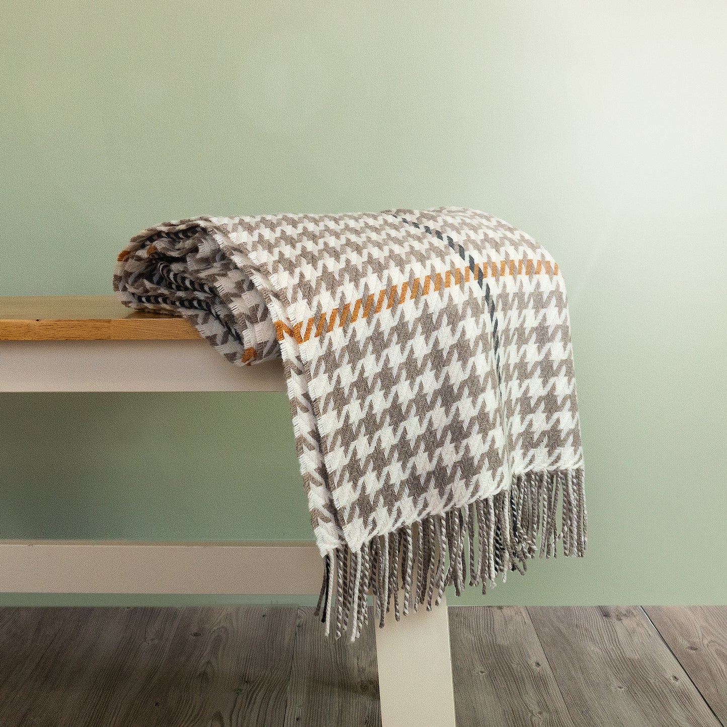 The Carroglen Wool Throw in colour Mushroom is a brown and orange houndstooth pattern, shown folded on a bench.
