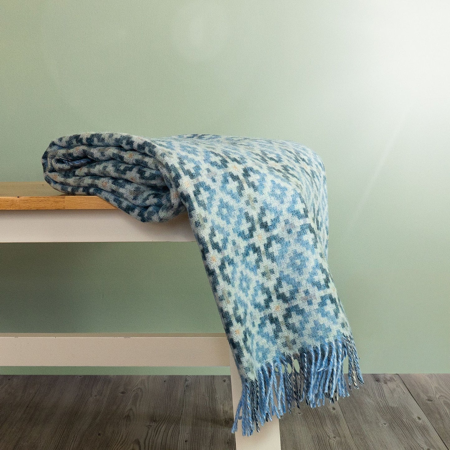 The Dartmouth Wool Throw in Blue is a unique cross and square pattern and fringe, shown folded on a bench.