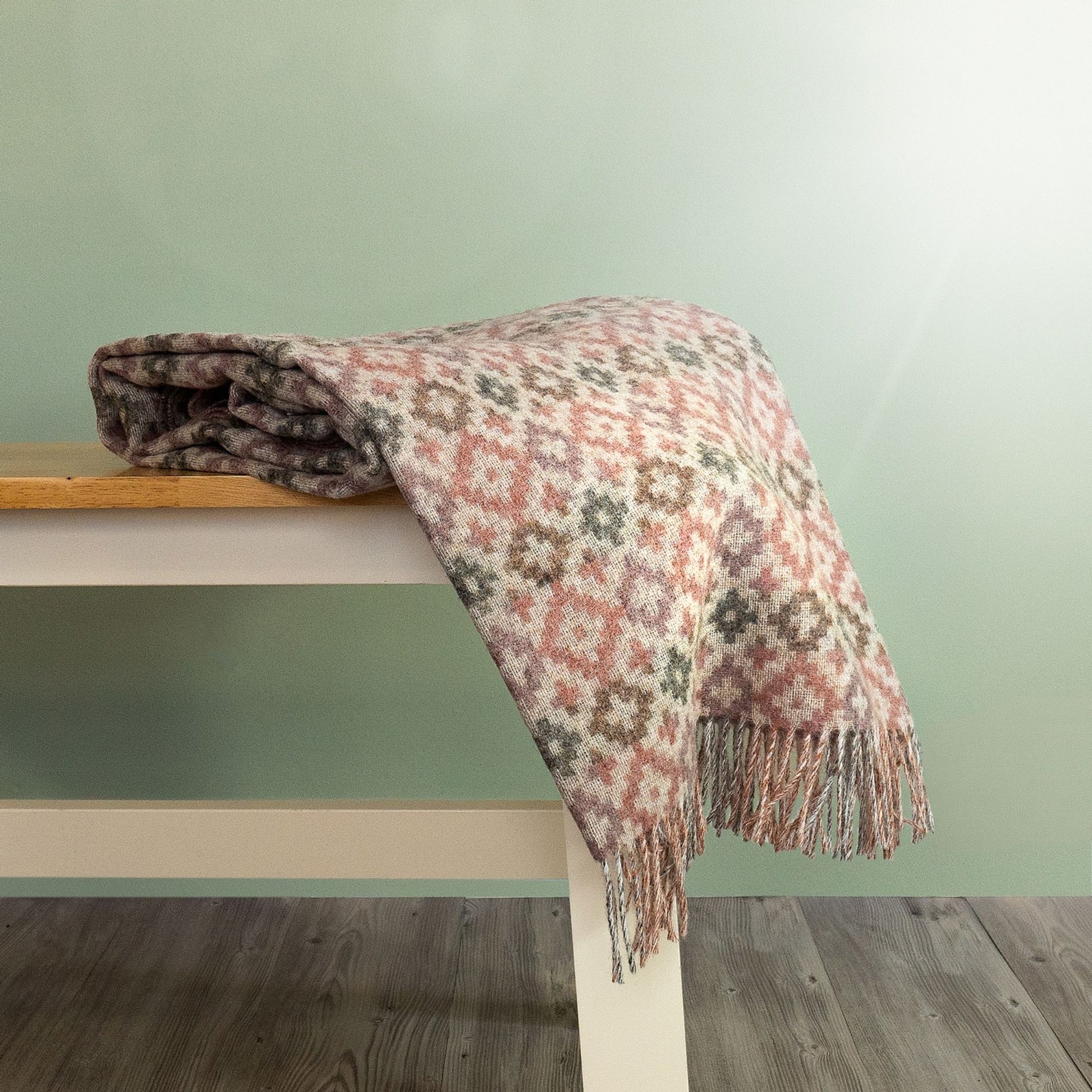 The Dartmouth Wool Throw in Coral is a unique cross and square pattern and fringe, shown folded on a bench.