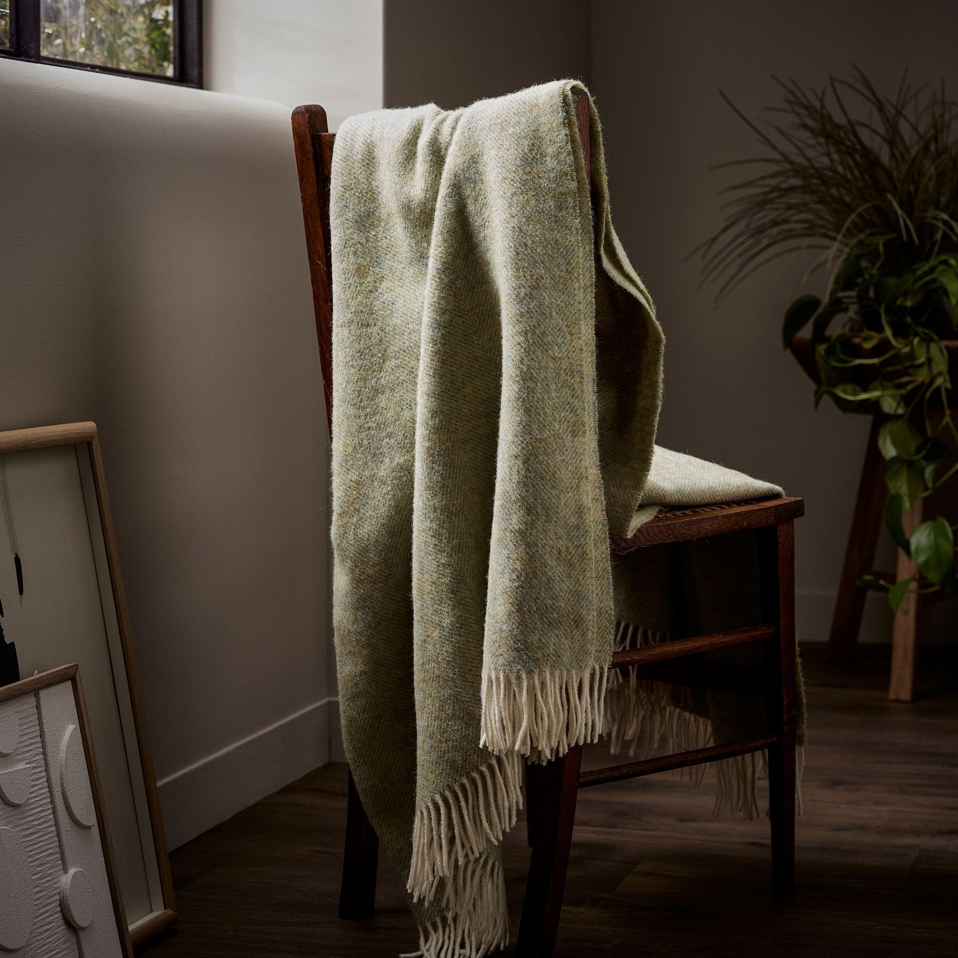 The beautifully soft Herringbone Shetland Wool Throw in colour Light Sage with white fringe, draped over a bench.
