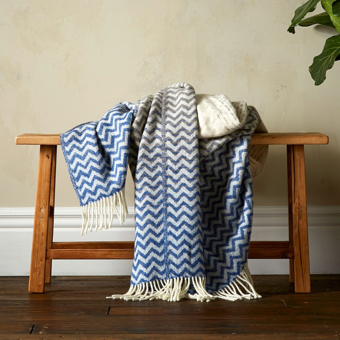 The Woolroom Astrid Gradient Pure New Wool Throw in colour Blue, draped on a bench with fringe.