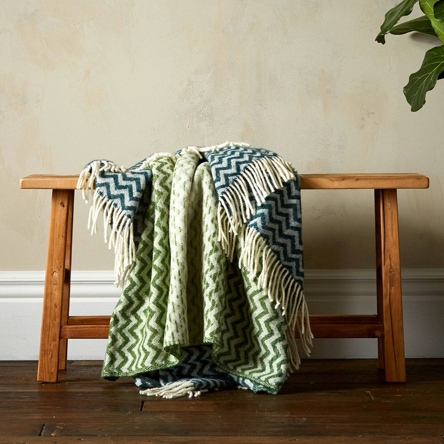 The Woolroom Astrid Gradient Pure New Wool Throw in colour Green, draped on a bench with fringe.