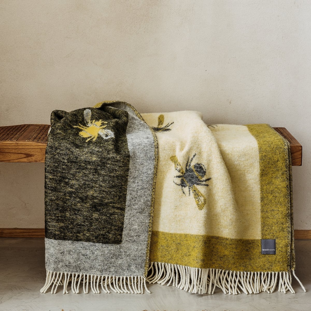 The popular Woolroom Wild and Wool Bee Wool Throw in Yellow and Black showing the white fringe and bee pattern on a bench.