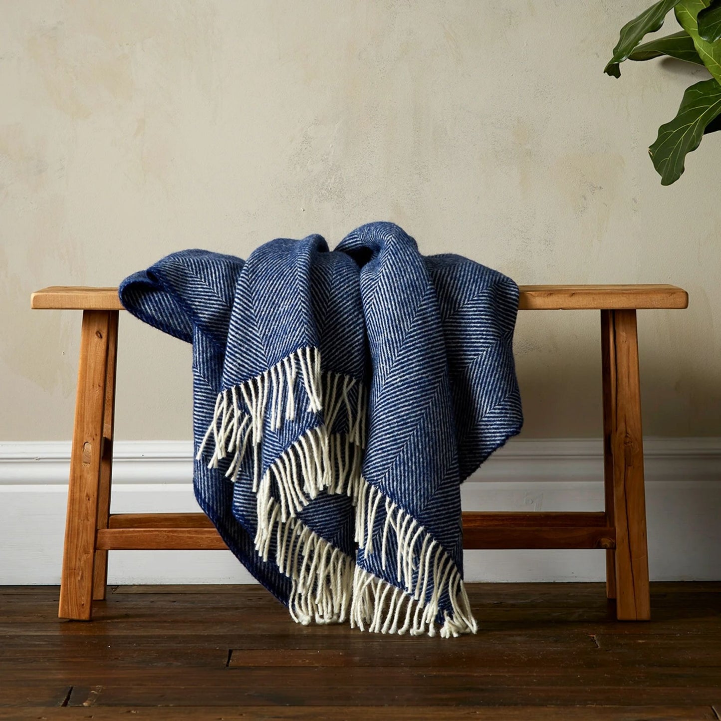 The super soft Greta Herringbone Wool Blanket in Navy draped over a bench with white fringe.