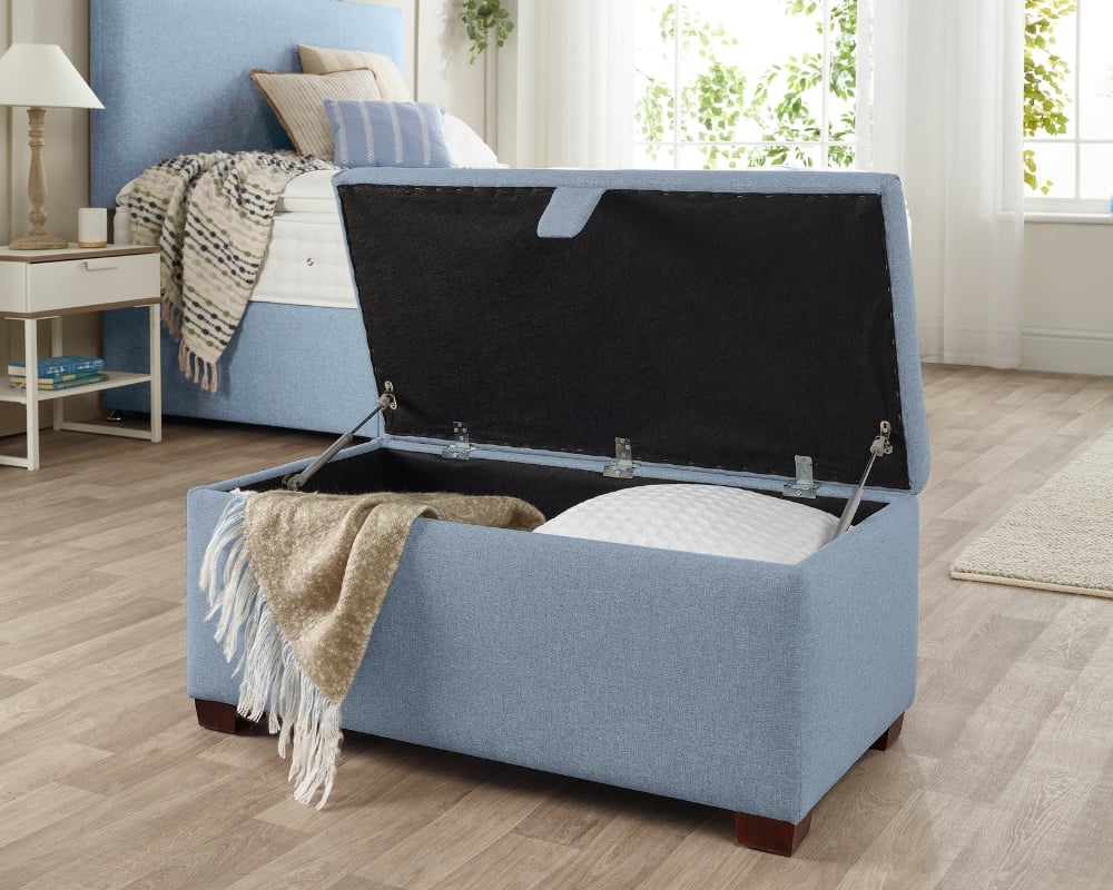 Blue storage ottoman with open lid in a bedroom setting
