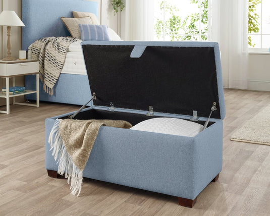 Blue storage ottoman with open lid in a bedroom setting