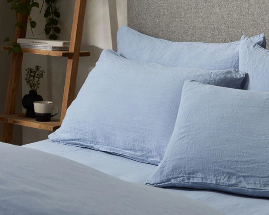 Blue textured bed sheets and pillows on a bed with a wooden nightstand in the background.