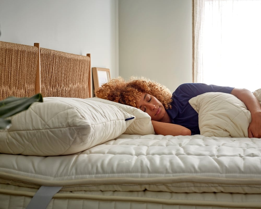 Woman lying on a bed with white bedding and pillows in a bedroom setting.