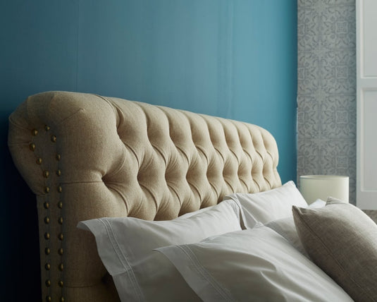 Beige tufted headboard with white bedding against a blue wall