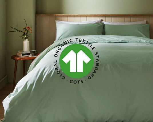 Green bedding set on a bed with a visible Global Organic Textile Standard logo.