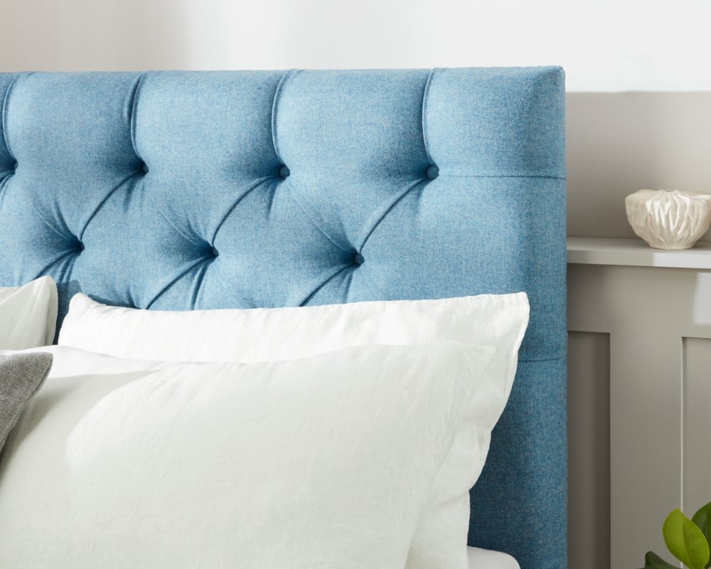 Blue tufted headboard with white pillows against a neutral wall.