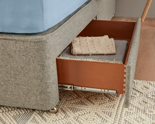 Open drawer of a gray upholstered furniture piece with folded blankets inside, on a textured carpet.