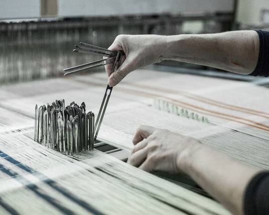 Person working with tools on a loom in a textile factory.