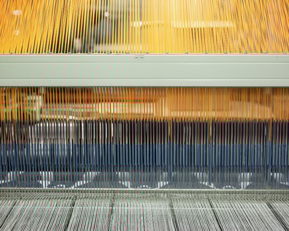 Close-up of a textile loom with threads and metal components.