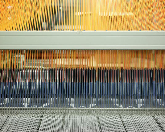 Close-up of a textile loom with threads and metal components.