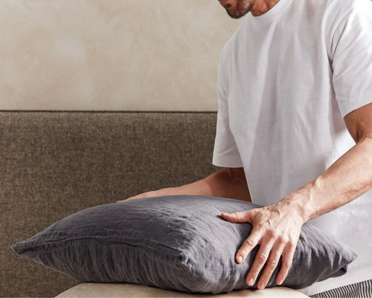 Person holding a gray pillow against a neutral background