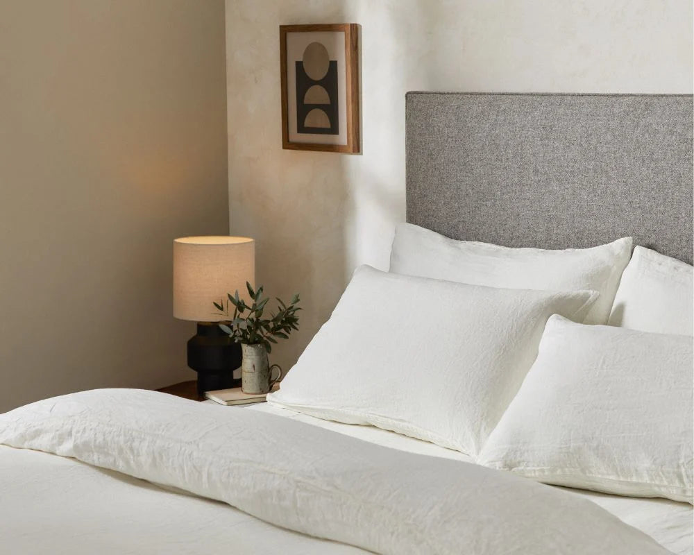 Neatly made bed with white bedding and gray headboard in a bedroom setting.
