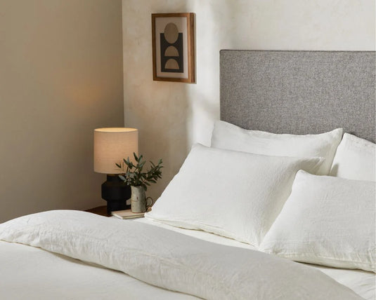 Neatly made bed with white bedding and gray headboard in a bedroom setting.