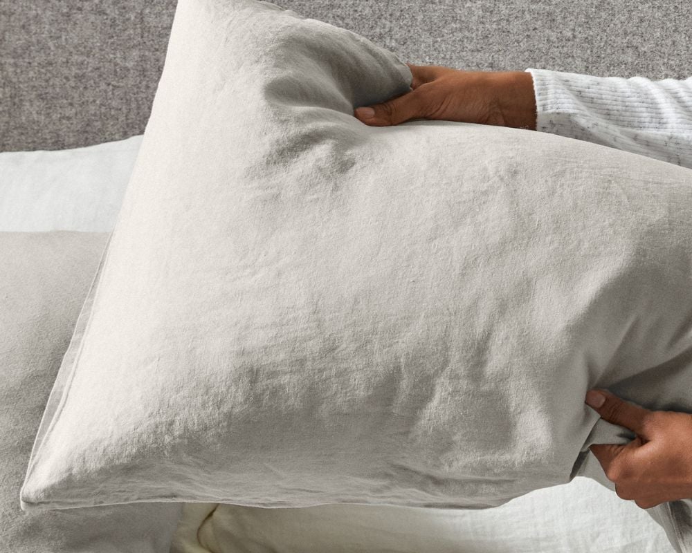 Person holding a gray pillow against a neutral background