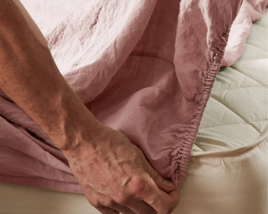 Person adjusting a pink fitted sheet on a bed