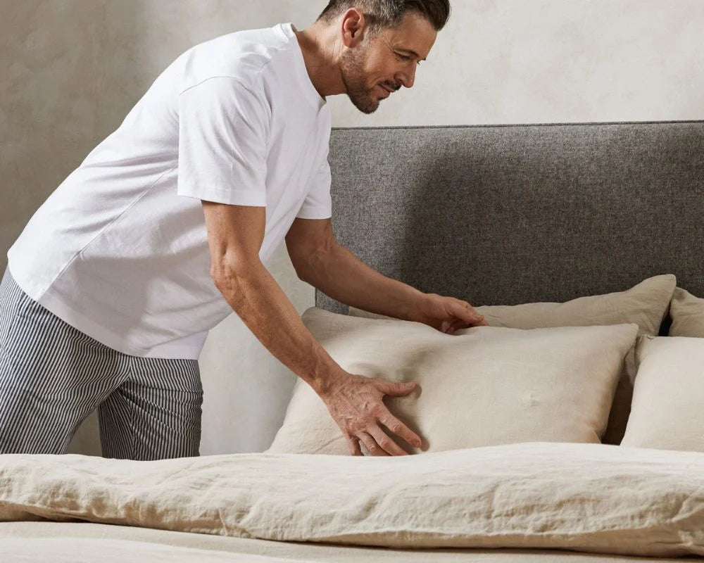 Man arranging pillows on a bed in a bedroom setting