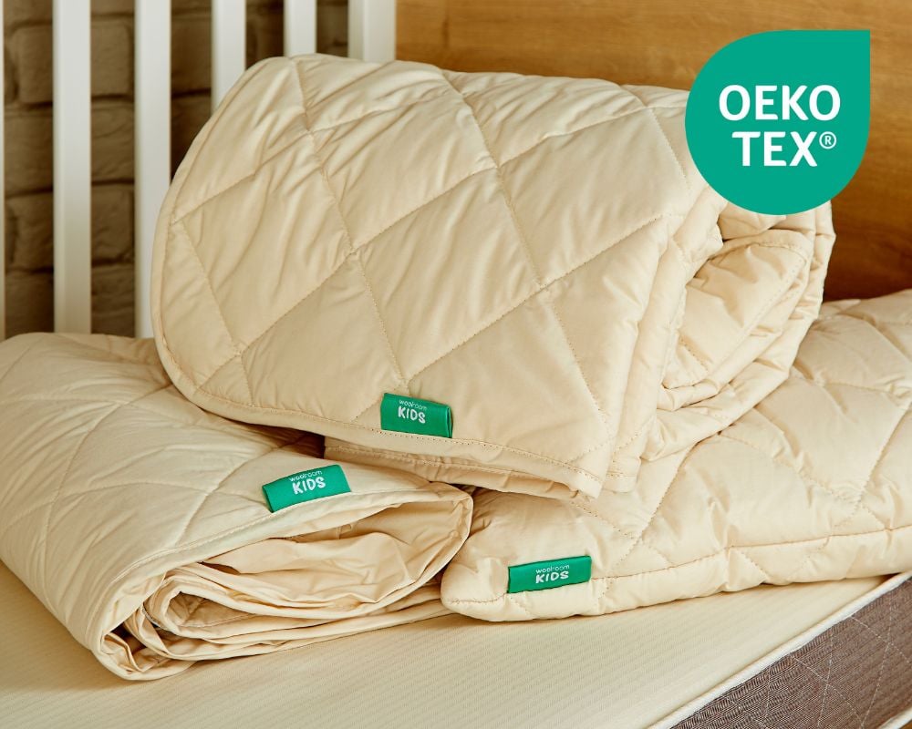 Beige kids quilt with OEKO-TEX labels on a bed