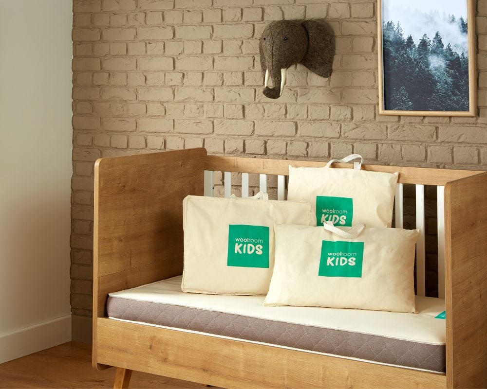 Wooden crib with pillows featuring Woolroom branding against a brick wall.