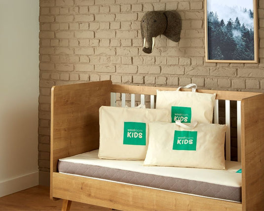 Wooden crib with pillows featuring Woolroom branding against a brick wall.