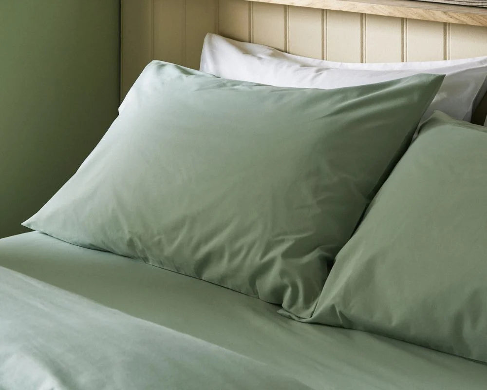 Green bed sheets and pillows on a bed with a wooden headboard.