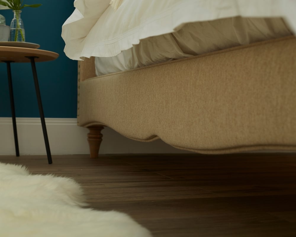 Beige bed in a bedroom with a blue wall and wooden floor.