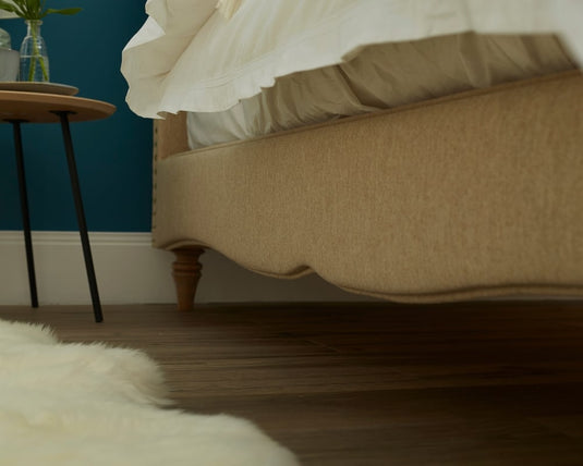 Beige bed in a bedroom with a blue wall and wooden floor.