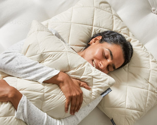 Person lying on a white comforter with a pillow, smiling.