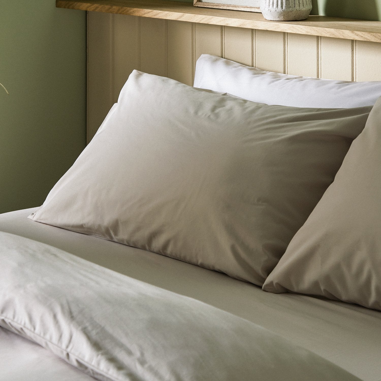The crisp Arinta Organic Cotton Pillow Case in Almond on a dressed bed with four pillows.