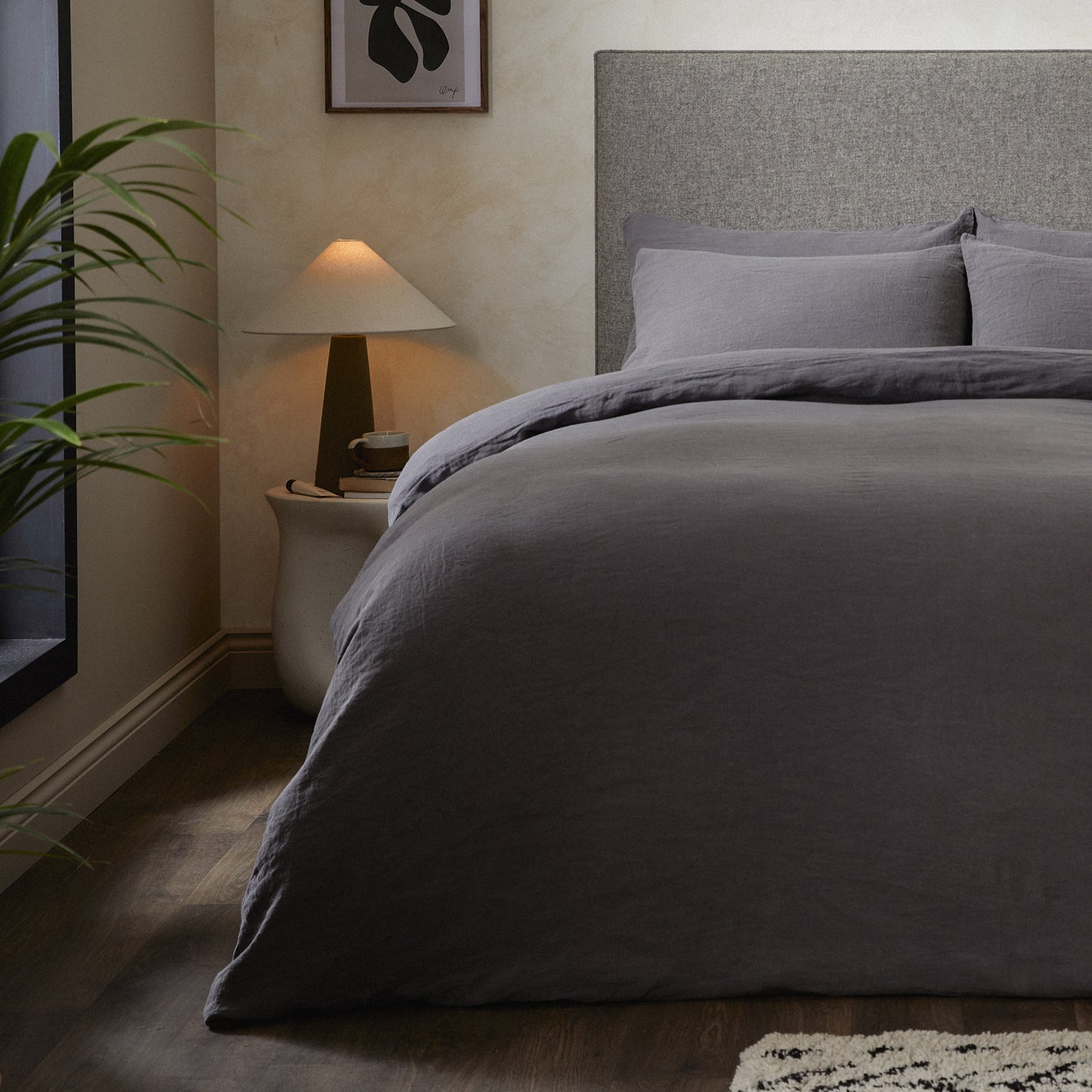 A dressed bed with Woolroom's Mariana Linen Comforter Cover in Charcoal has the comforter turned down and two pillows.