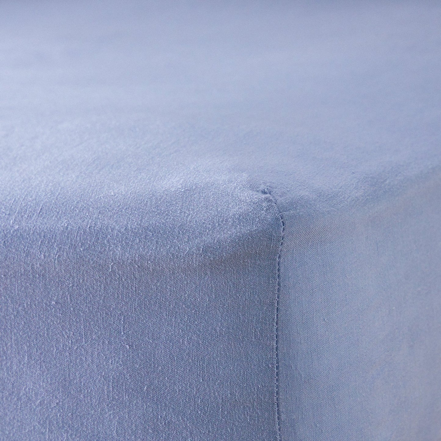 A close up of the corner of a mattress with Woolroom's Mariana Linen Blend Fitted Sheet in Cornflower.