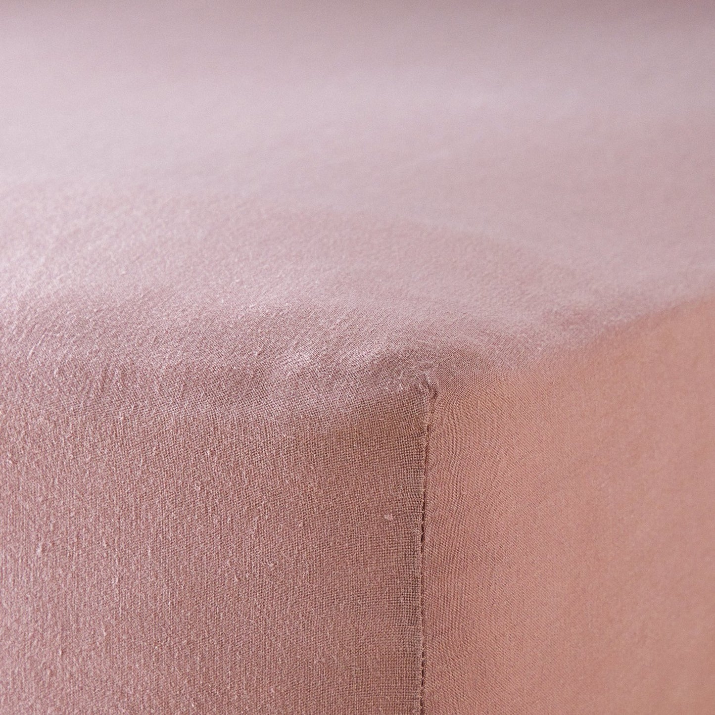 A close up of the corner of a mattress with Woolroom's Mariana Linen Blend Fitted Sheet in Rose.