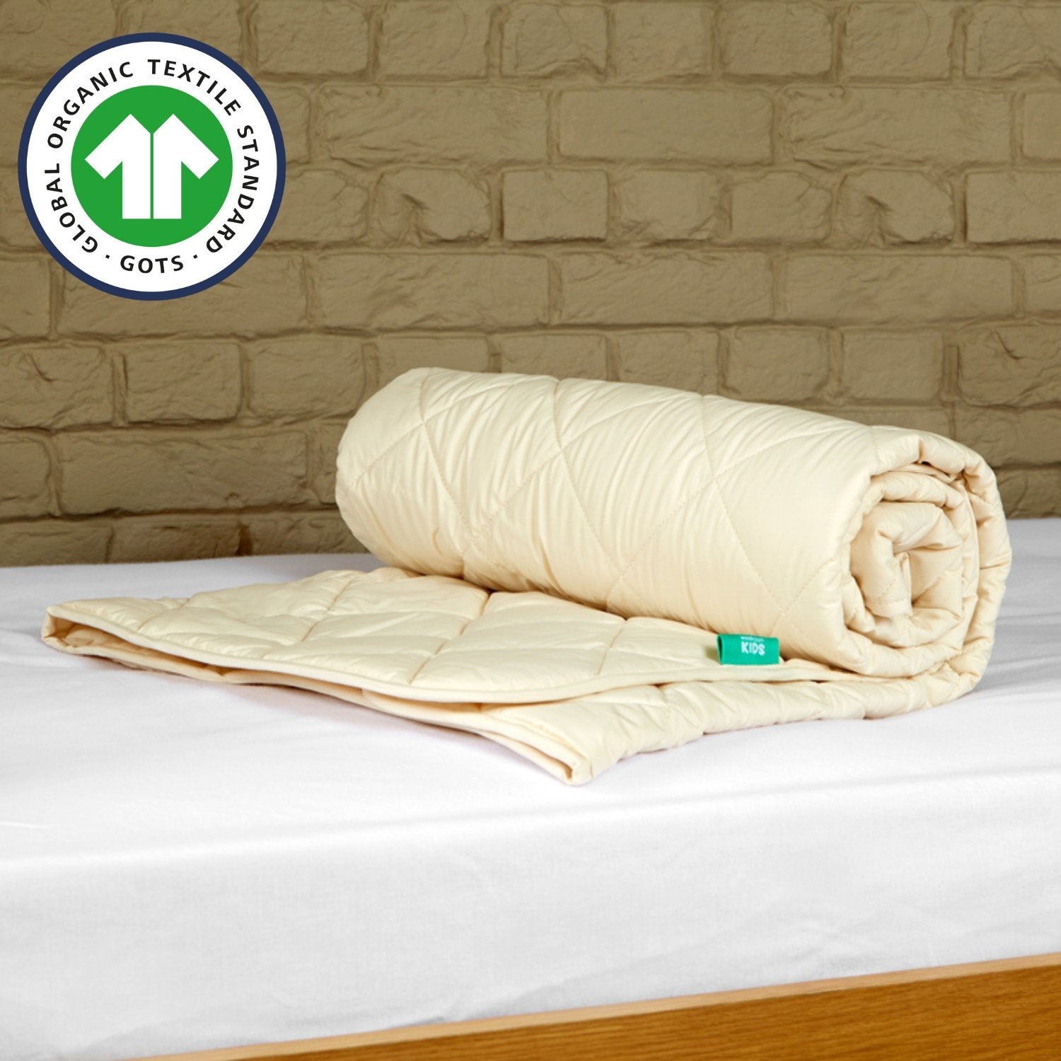 The Woolroom GOTS Organic Washable Wool Comforter for a crib rolled up and on a kids mattress with a white fitted sheet.
