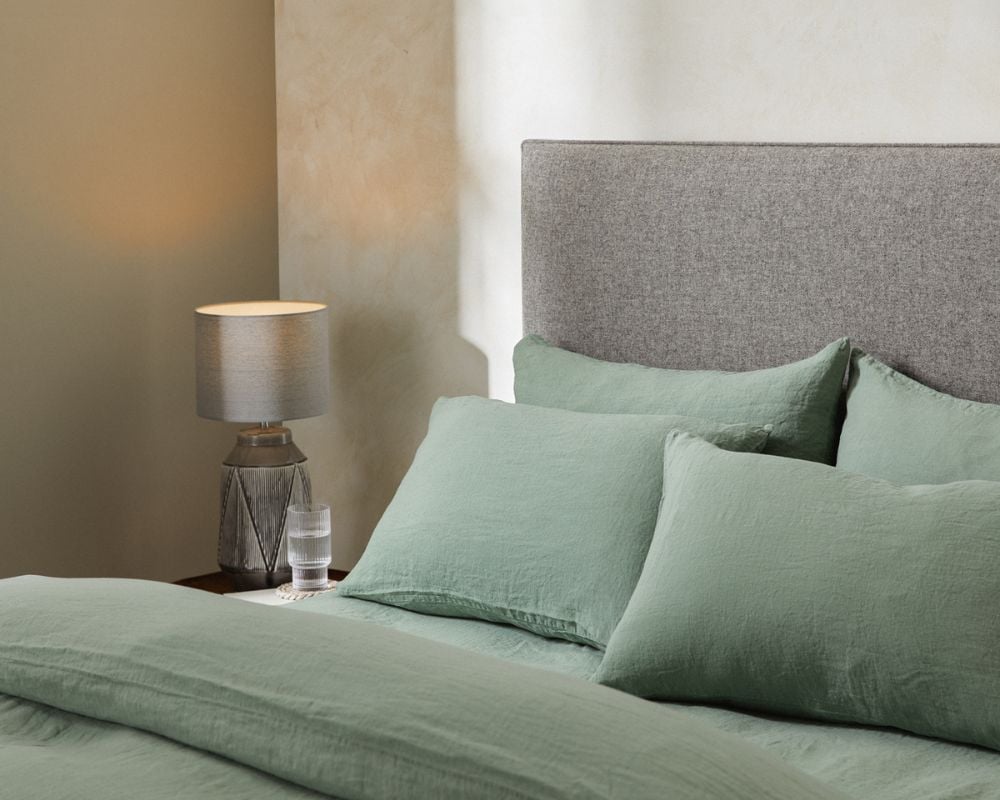Bed with green bedding and gray headboard, nightstand with lamp and glass.