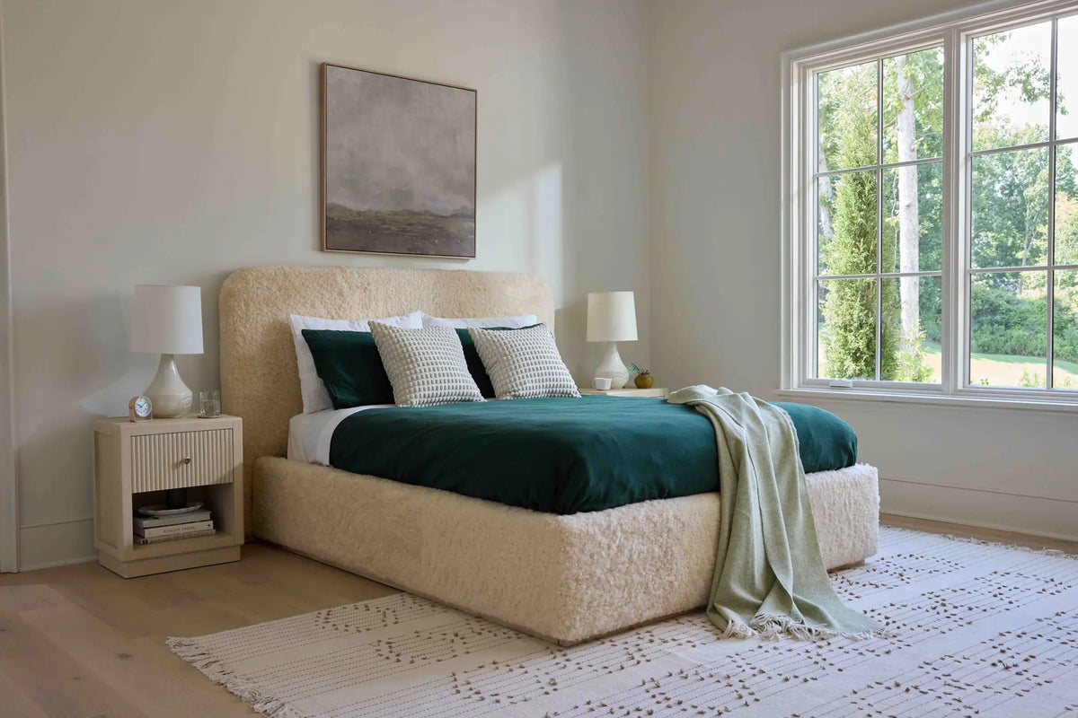 Sculptural Charlotte bed with cream shearling headboard and green bedding on a plinth base