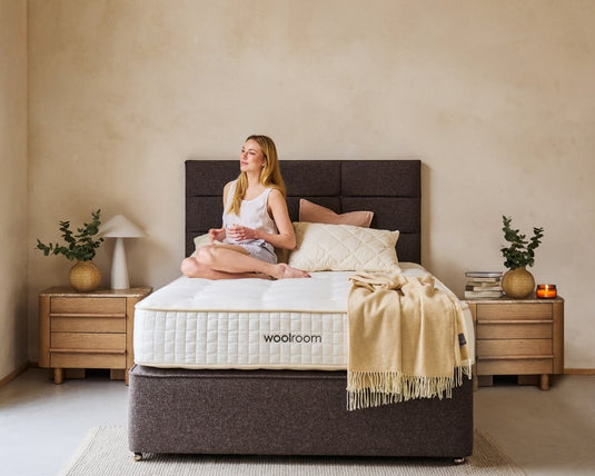 Woman sitting on a bed with 'woolroom' mattress in a cozy bedroom setting