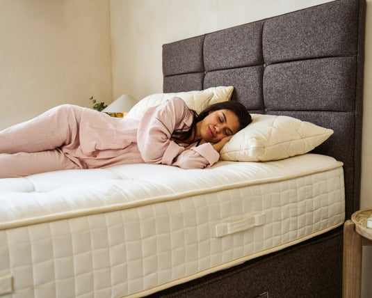 Woman lying on a mattress in a bedroom with a gray upholstered headboard.