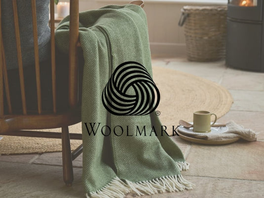 Green blanket draped over a chair with a Woolmark logo in a cozy indoor setting.
