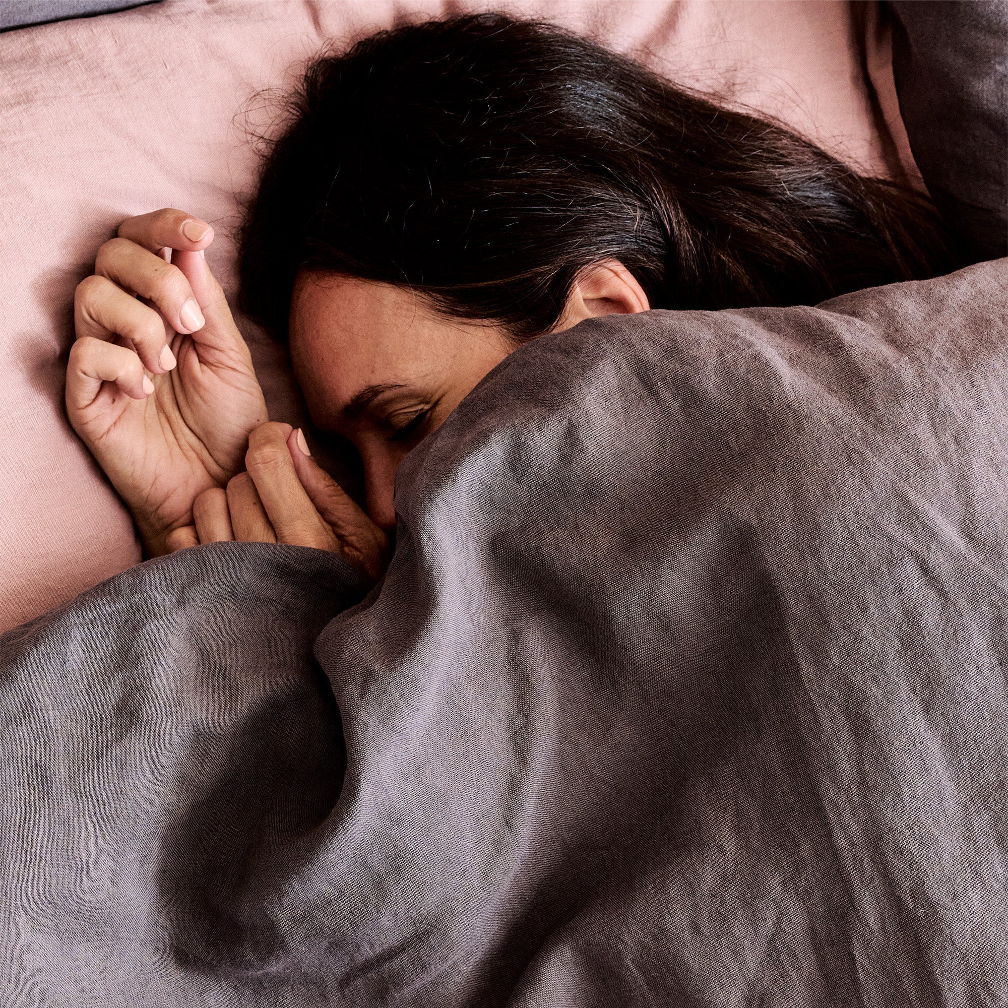 A woman is fast asleep in a bed with woolroom mariana linens (charcoal and rose coloured)