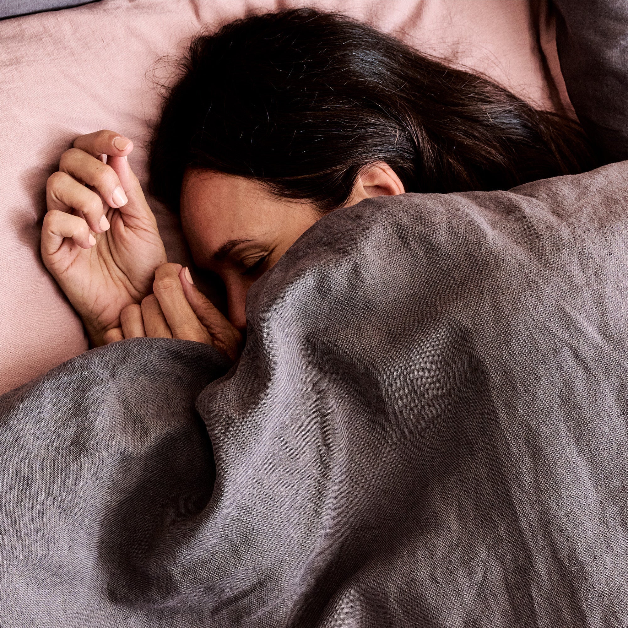 A woman is fast asleep in a bed with woolroom mariana linens (charcoal and rose coloured)