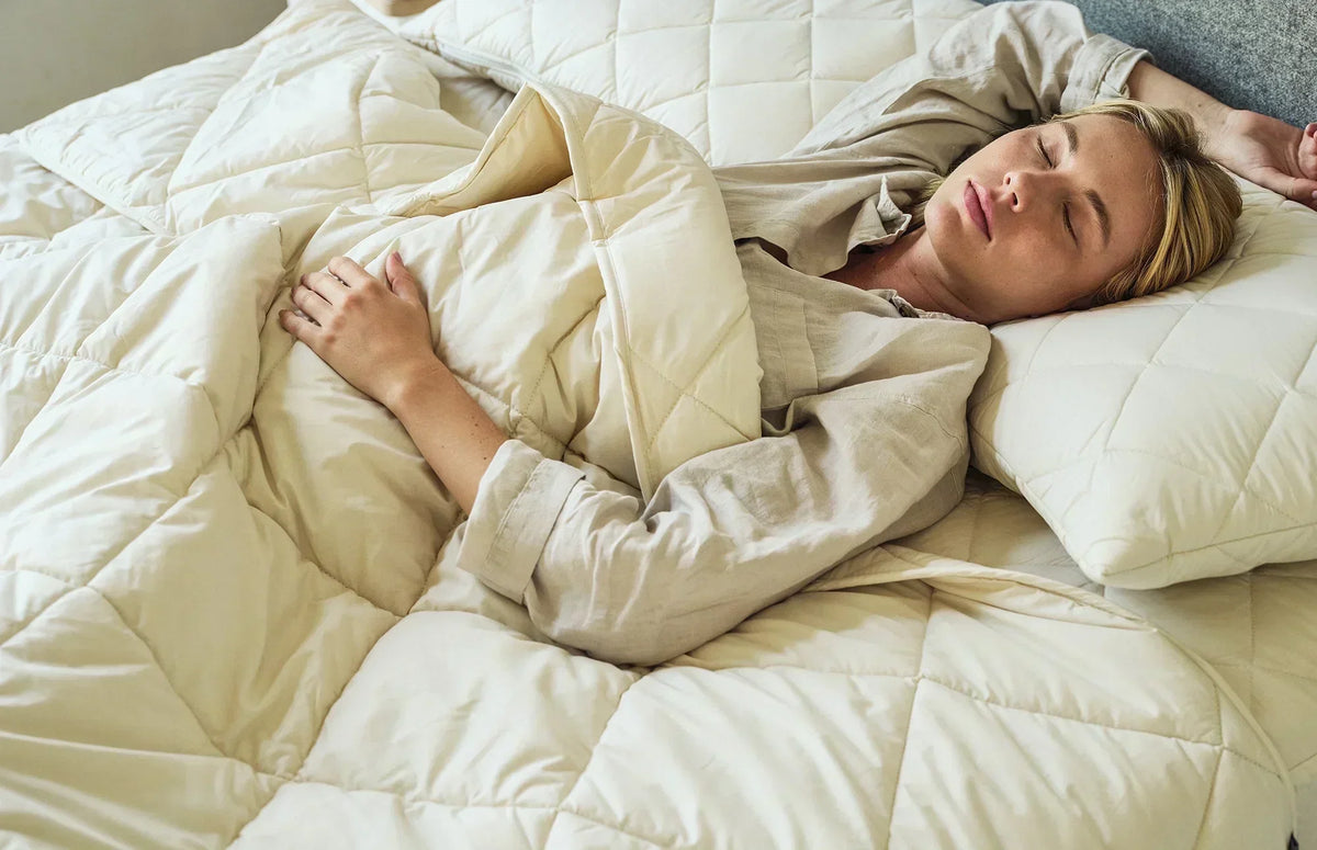Woman sleeping on her back, wrapped in a quilted cream wool comforter.
