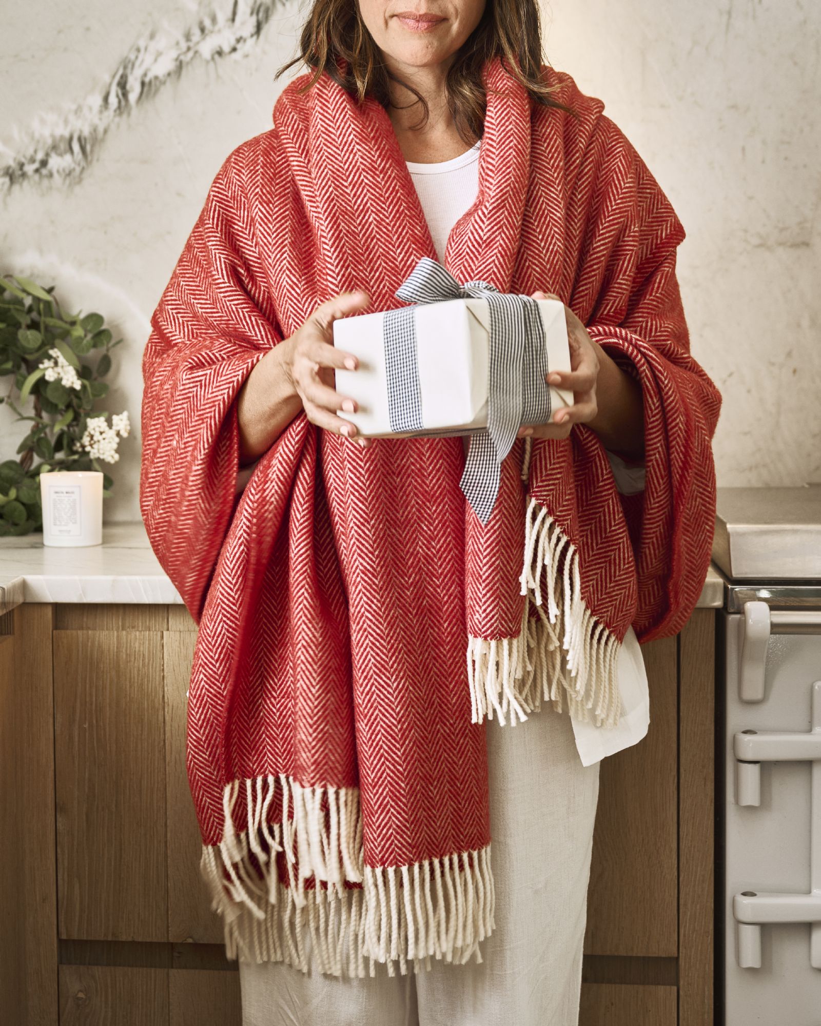 Woman holding a gift for the holidays, and she is wrapped in a cozy red Woolroom wool throw blanket.